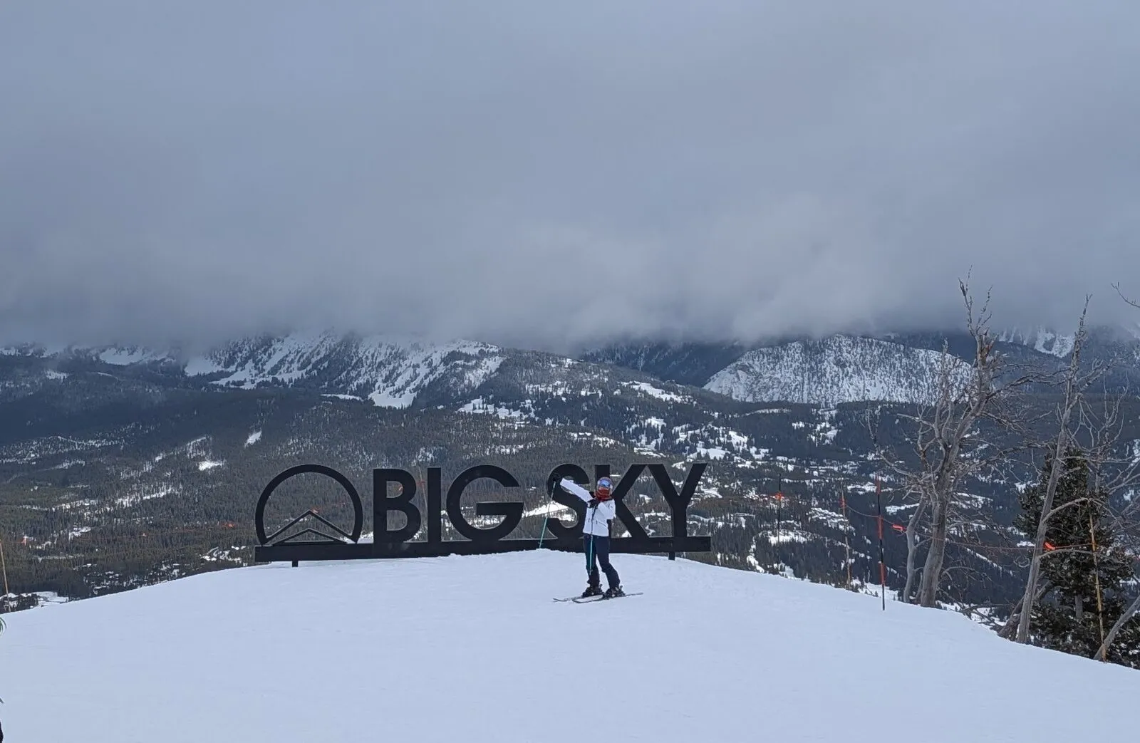 A lone skier under the Big Sky sign, with low cloud and dark, thinly covered mountainsides behind.