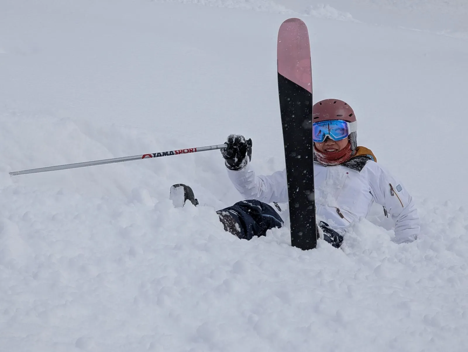 Buried to the chest in deep powder, one ski pointing straight up, pole and glove flung out.